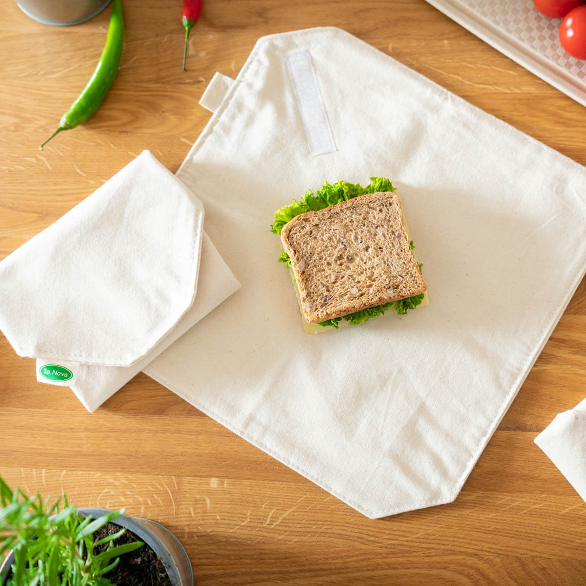 Nachhaltiger Lunch Wrap von Io Nova liegt geöffnet auf einem Holztisch, mit einem belegten Vollkornbrot und weiteren Wraps im Hintergrund.
