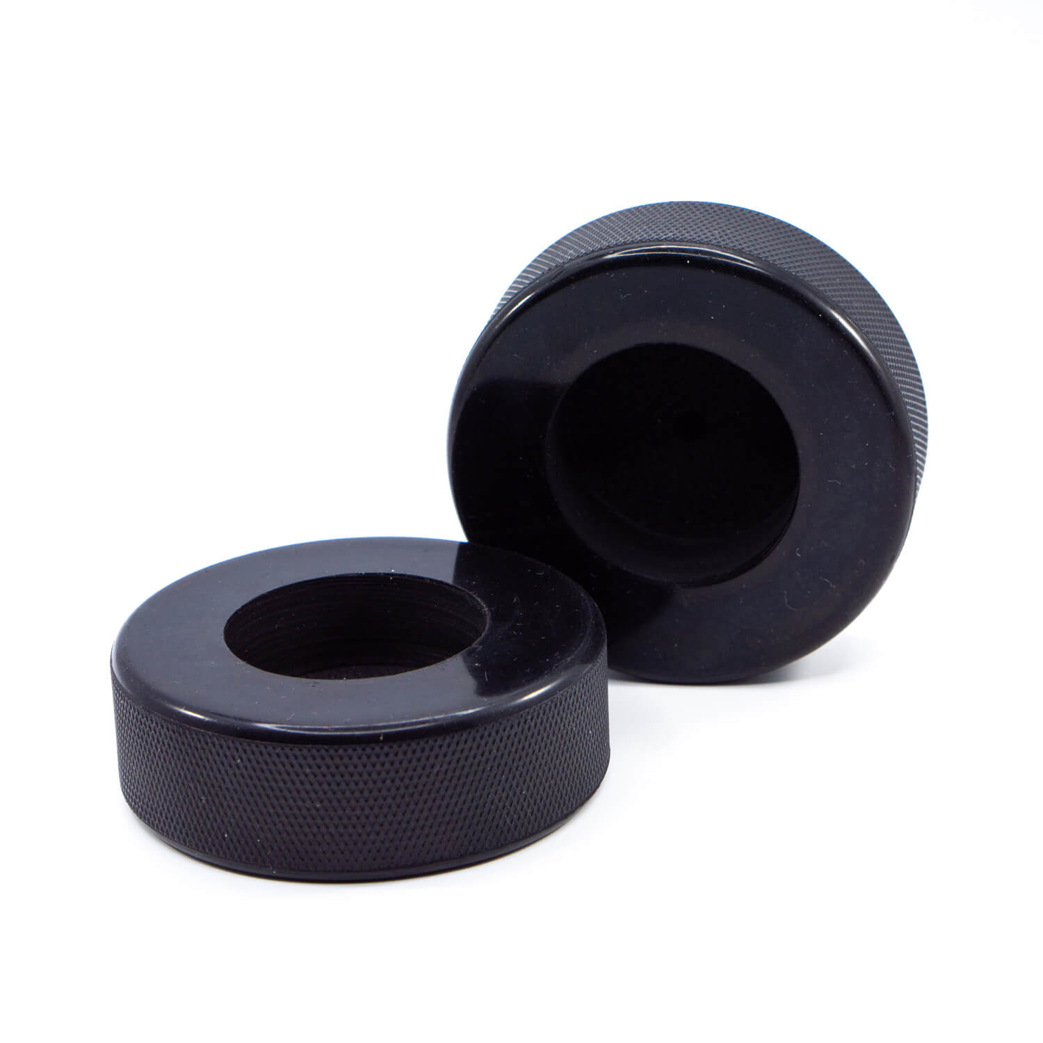 Zwei schwarze Teelichthalter aus recycelten Eishockey-Pucks auf weißem Hintergrund – ohne Teelicht.