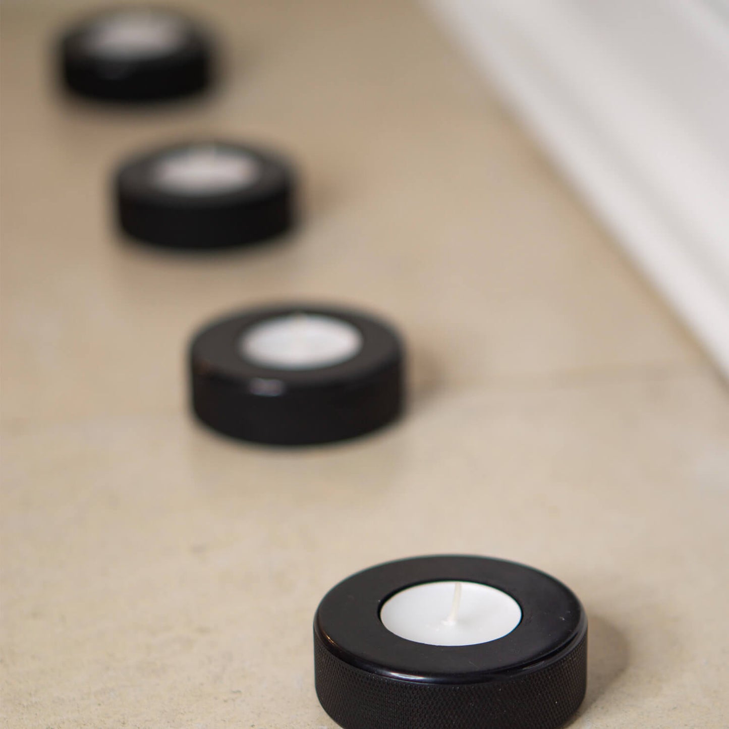 Vier schwarze Teelichthalter aus recycelten Eishockey-Pucks in einer Reihe auf einem hellen Boden – sportliches Upcycling für stimmungsvolle Deko.