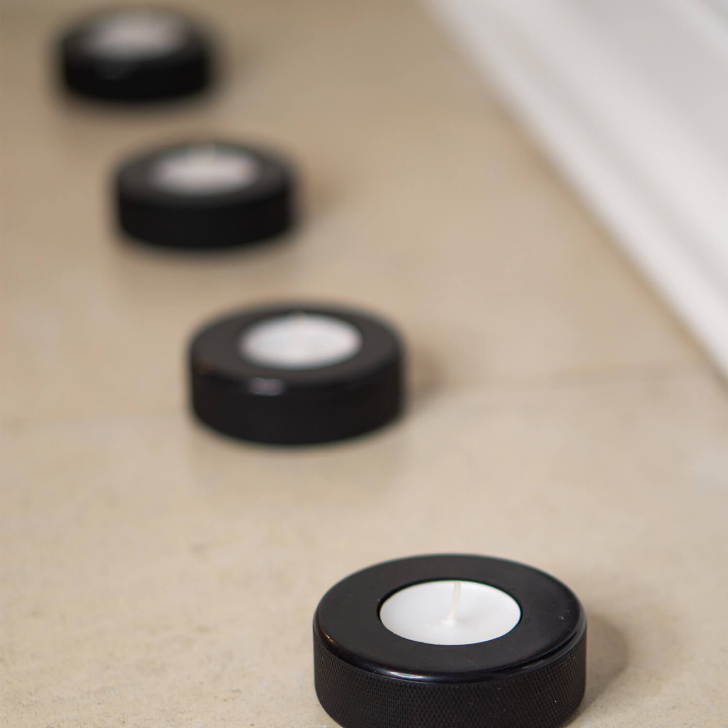 Vier schwarze Teelichthalter aus recycelten Eishockey-Pucks in einer Reihe auf einem hellen Boden – sportliches Upcycling für stimmungsvolle Deko.
