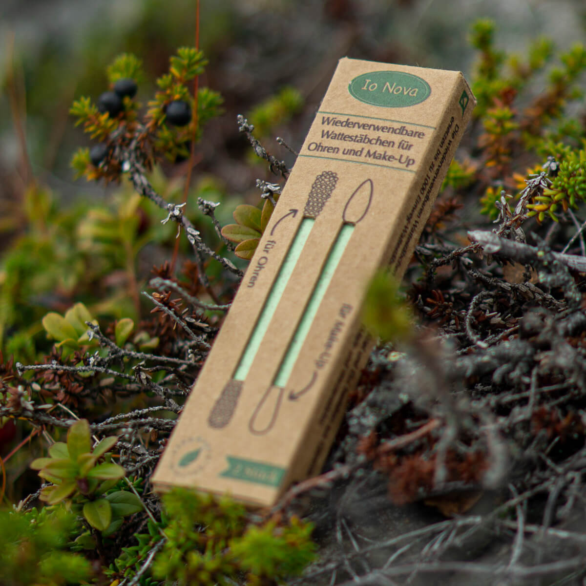 Verpackung der wiederverwendbaren Wattestäbchen von Io Nova liegt auf Moos und Zweigen in der Natur.