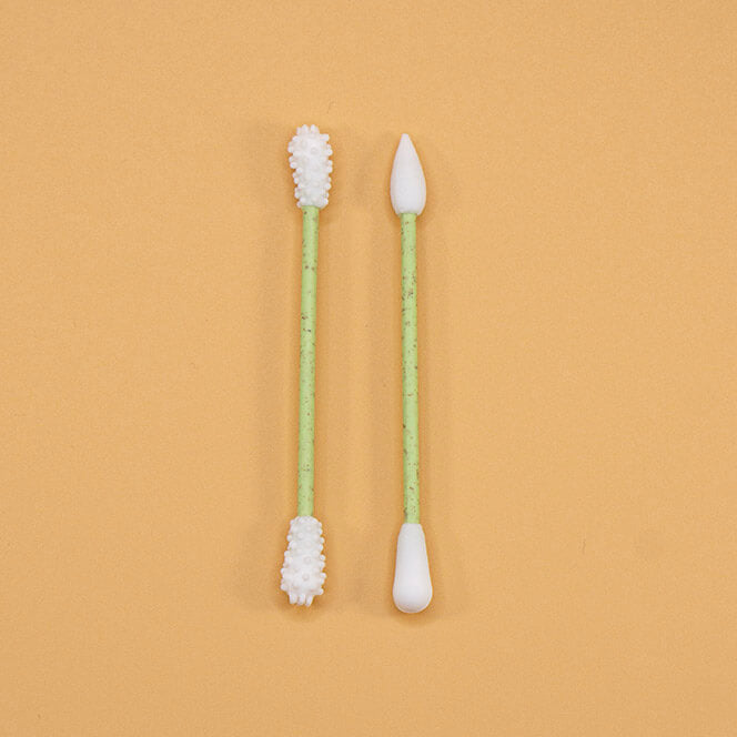Zwei wiederverwendbare Wattestäbchen mit grünem Stiel und weißen Enden – nebeneinander auf orangefarbenem Hintergrund.