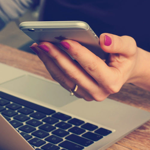 Frauenhand hält ein iPhone in der linken Hand und sitzt an einem MAC