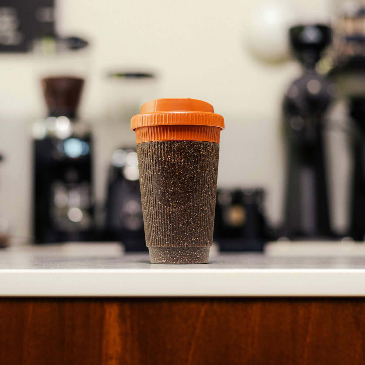 Nachhaltiger Coffee-to-go Becher aus Kaffeesatz mit orangefarbenem Deckel auf Küchentheke – wiederverwendbarer Becher für umweltfreundlichen Kaffeegenuss.