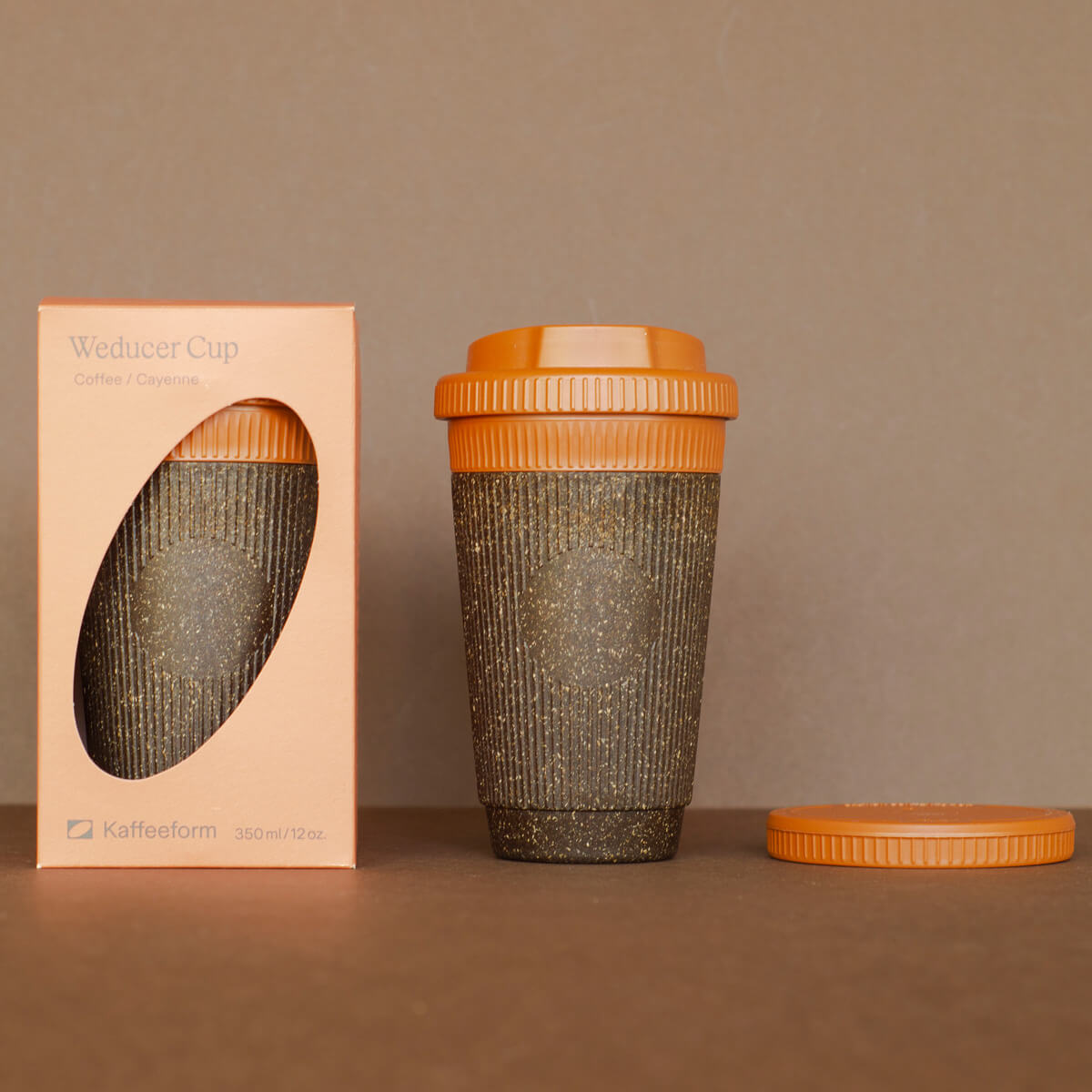 Nachhaltiger Coffee-to-go Becher aus Kaffeesatz mit orangefarbenem Deckel neben Verpackung – wiederverwendbarer Kaffeebecher umweltfreundlich.