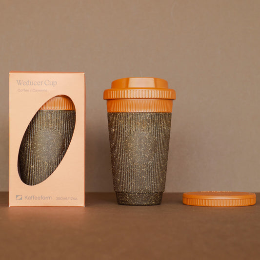 Nachhaltiger Coffee-to-go Becher aus Kaffeesatz mit orangefarbenem Deckel neben Verpackung – wiederverwendbarer Kaffeebecher umweltfreundlich.